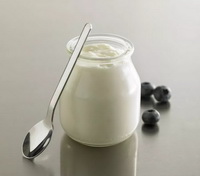 a bottle of Yogurt with a small spoon and several blueberry fruits